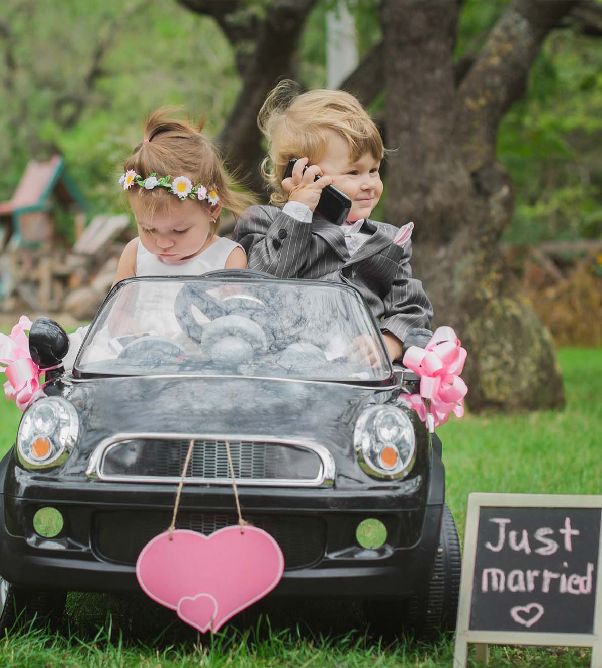Image of two adorable kids playfully imitating a married couple in a mini car, symbolising the fun and whimsical aspects discussed in Ash Reynolds' FAQs.